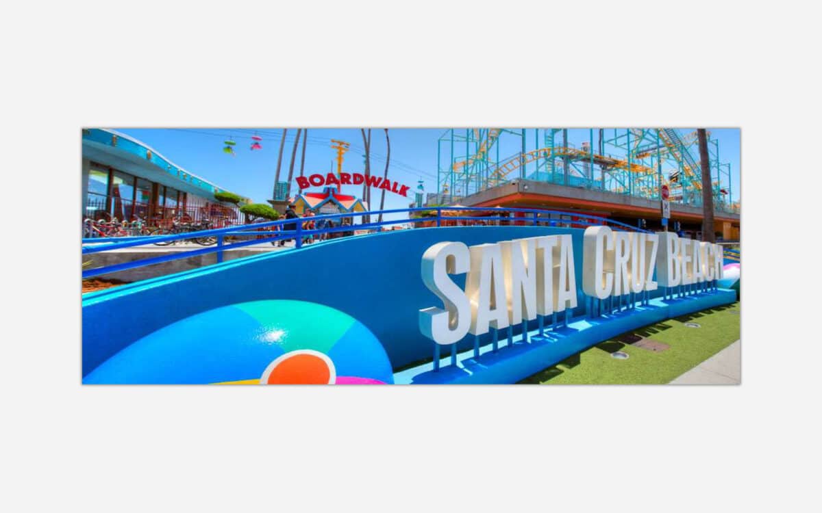 A colorful image of Santa Cruz Beach Boardwalk with clear blue skies and amusement park attractions in the background.