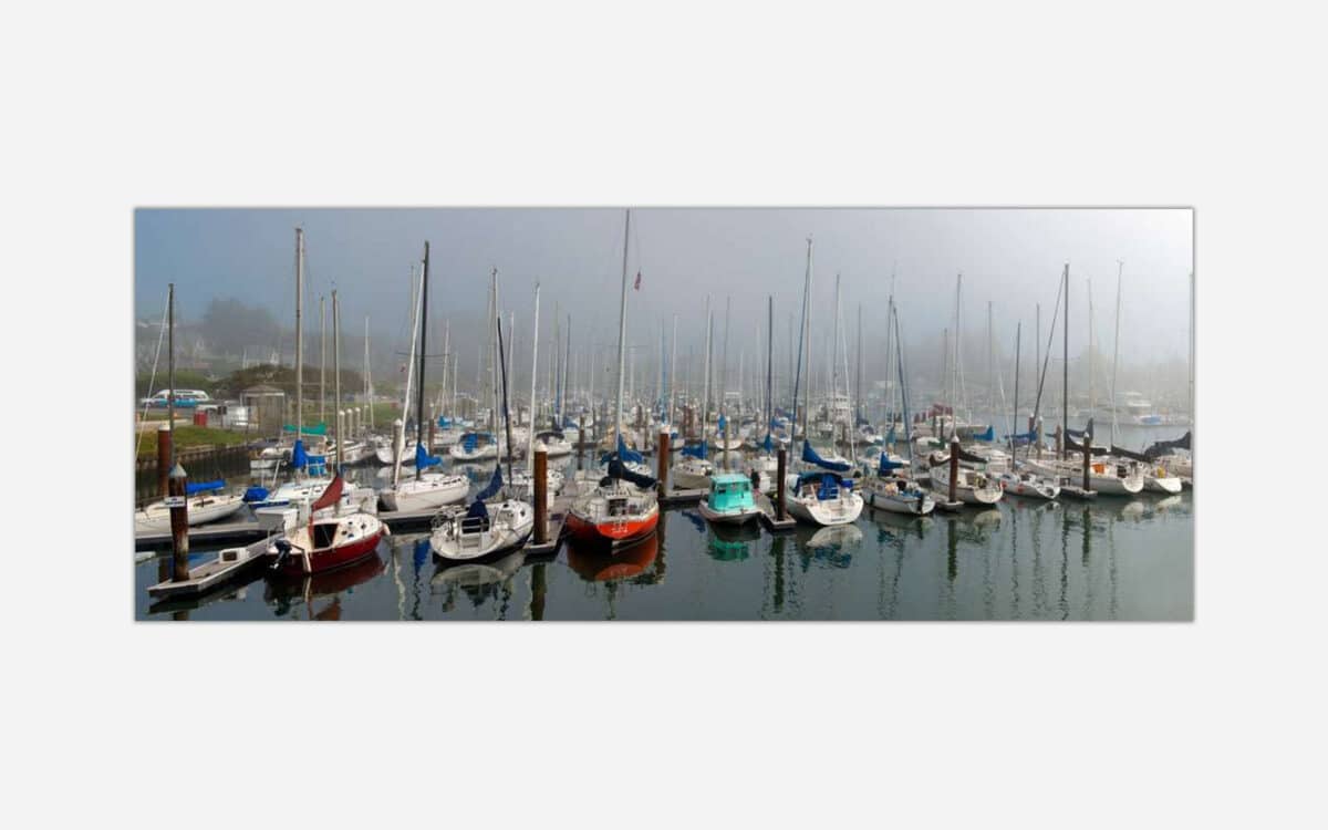 A serene artwork displaying a foggy marina with multiple sailboats docked and their reflections in the calm water.