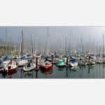 A serene artwork displaying a foggy marina with multiple sailboats docked and their reflections in the calm water.