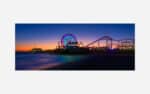 A photograph of a beach pier amusement park at sunset with a colorful Ferris wheel and roller coaster silhouettes against a twilight sky.