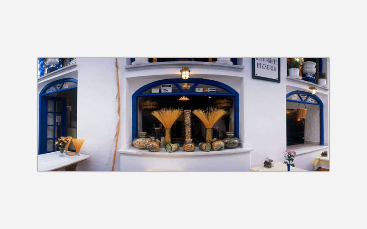 An artistic photograph of a charming Italian pizzeria with blue window frames, displayed pasta, and a traditional Mediterranean aesthetic.