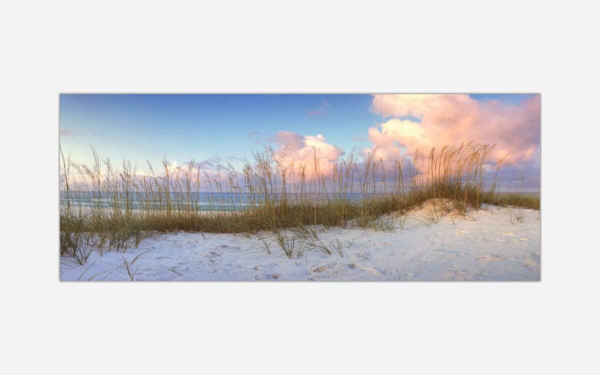 A photograph of a tranquil beach scene with sand dunes, sea oats, and a pastel-colored sky during sunset.