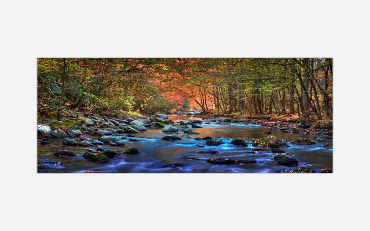 A photographic print depicting a serene autumn landscape with a flowing stream surrounded by colorful trees and scattered rocks.