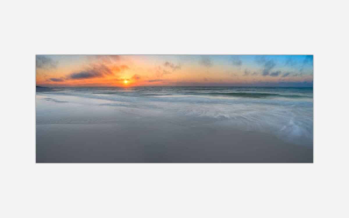 A panoramic photo of a serene beach at sunset with vibrant colors in the sky and gentle waves in the foreground.