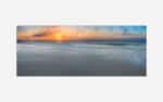 A panoramic photo of a serene beach at sunset with vibrant colors in the sky and gentle waves in the foreground.