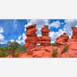 A high dynamic range photograph of distinctive red rock formations with a lush green landscape and a dramatic blue sky with clouds in the background.