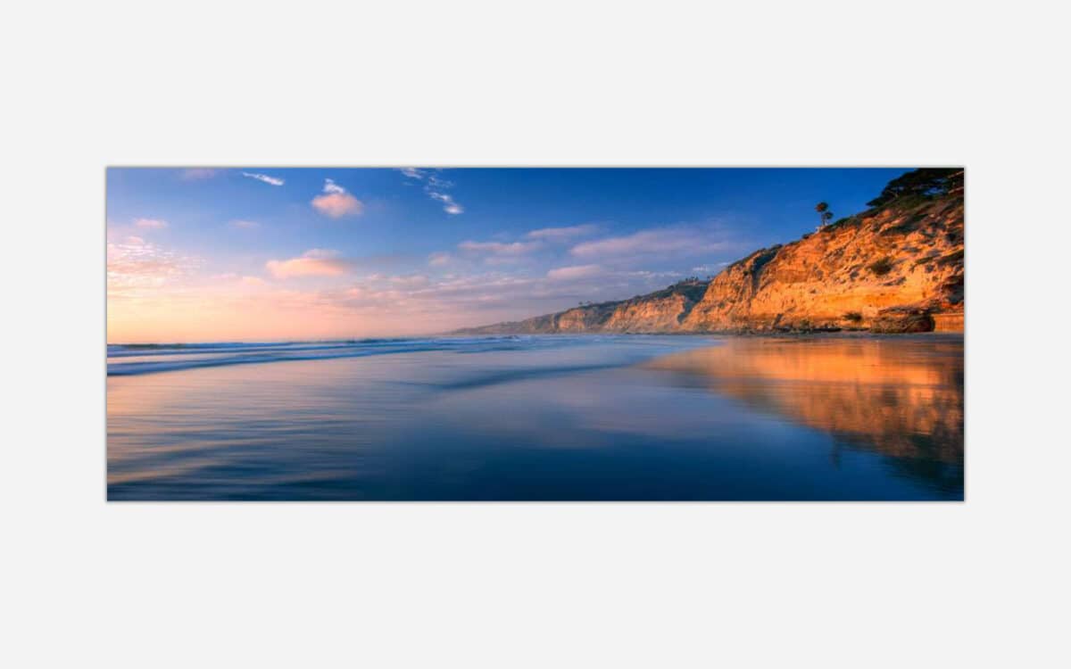 A serene coastal landscape at sunset with reflective ocean waters and a striking cliff formation on the right.