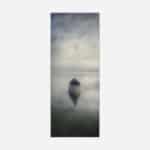 A serene monochrome photograph of a solitary boat on still water with a reflection and a calm, cloudy sky above.