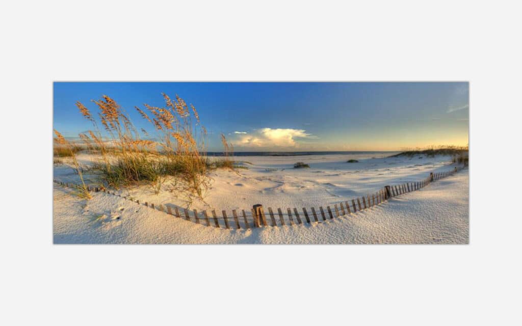 An image of a serene beach scene with sea oats, a wooden fence, white sandy dunes, and a beautiful sunset sky.