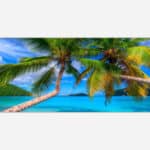 A vibrant art photograph of two coconut palm trees leaning over a serene tropical beach with clear blue water and a distant island under a bright blue sky.