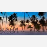 An art print of a serene beach sunset with silhouettes of palm trees and bicycles on white sand, under a pastel-colored sky.