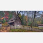 An image of an old wooden cabin surrounded by a rustic fence amidst trees with autumn foliage.