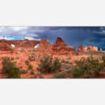 A panoramic photograph of Arches National Park with dramatic storm clouds and a lightning bolt in the distance over red desert rock formations.