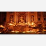 A nighttime photograph of the illuminated Trevi Fountain in Rome, showcasing its baroque sculptures and architecture.