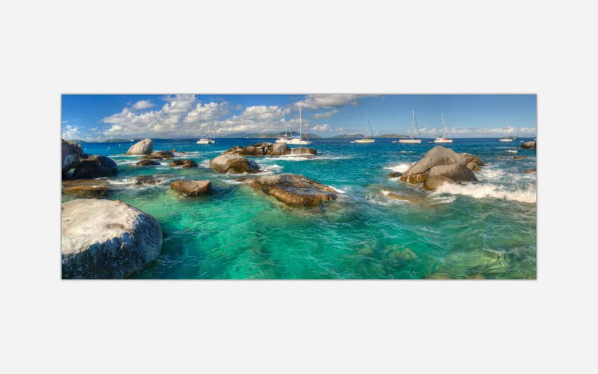 A panoramic canvas print depicting a vibrant turquoise sea with boulders, sailing yachts in the distance, and a clear blue sky.