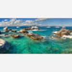 A panoramic canvas print depicting a vibrant turquoise sea with boulders, sailing yachts in the distance, and a clear blue sky.