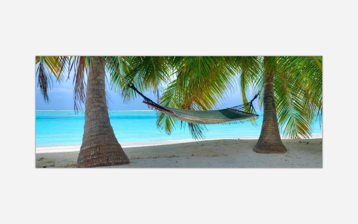 A hammock tied between two palm trees on a tranquil tropical beach with a clear turquoise sea in the background.