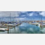 A painting of a serene marina with multiple docked boats under a cloudy blue sky.